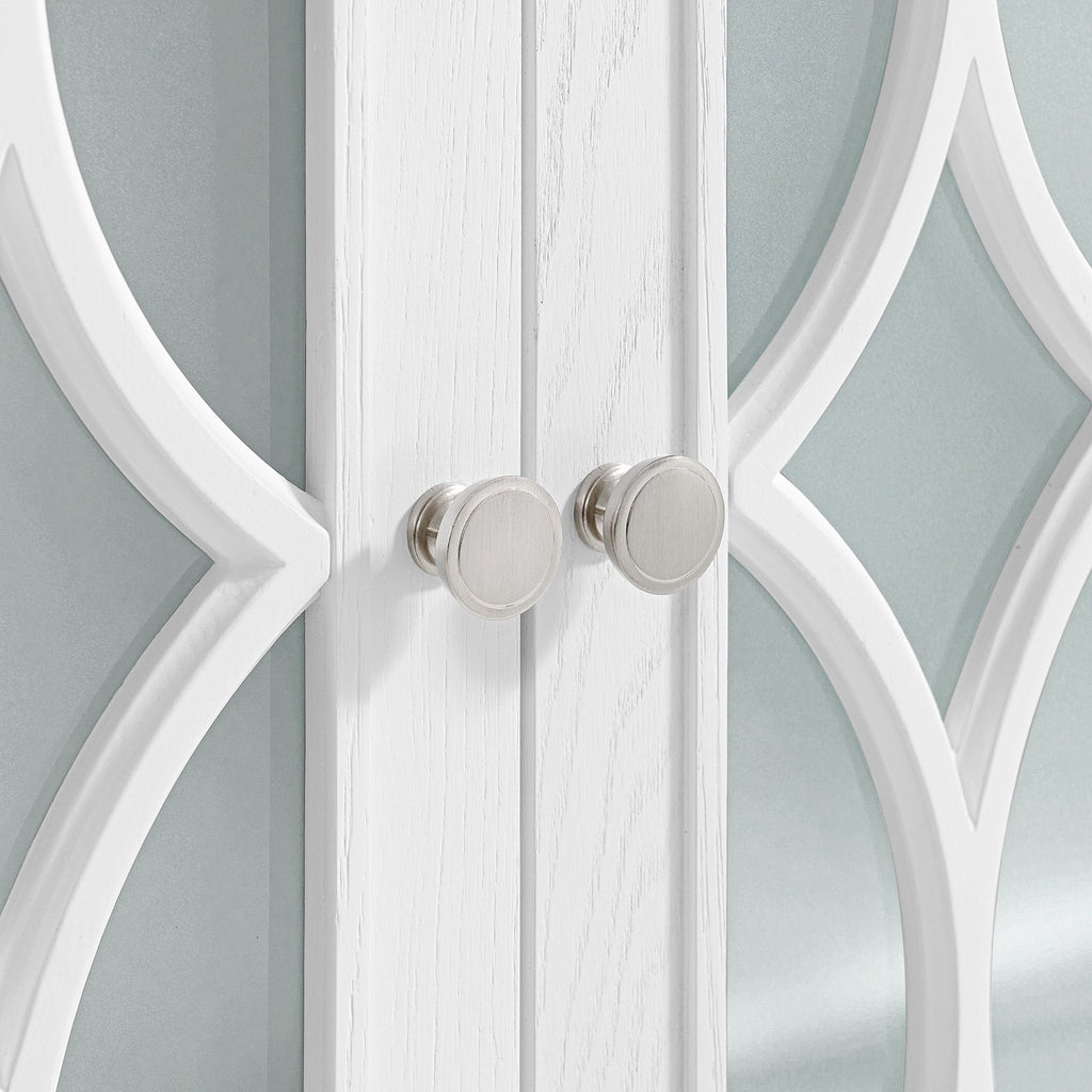 Close-up of modern white solid wood vanity doors with decorative arched trim and two round brushed-nickel knobs against a pale stone-toned mirrored background.