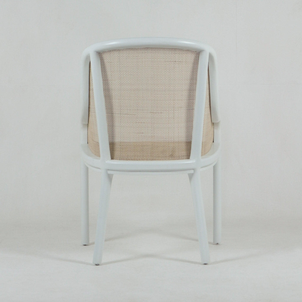 Rear view of a white bentwood dining chair with a curved frame, light beige woven cane back and seat, tapered legs and integrated arm supports in a modern mid-century style.