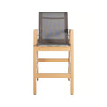 Front view of a teak outdoor bar stool with a natural finish wooden frame, gray mesh sling seat and back, squared armrests and integrated footrest, coastal-style counter-height seating.