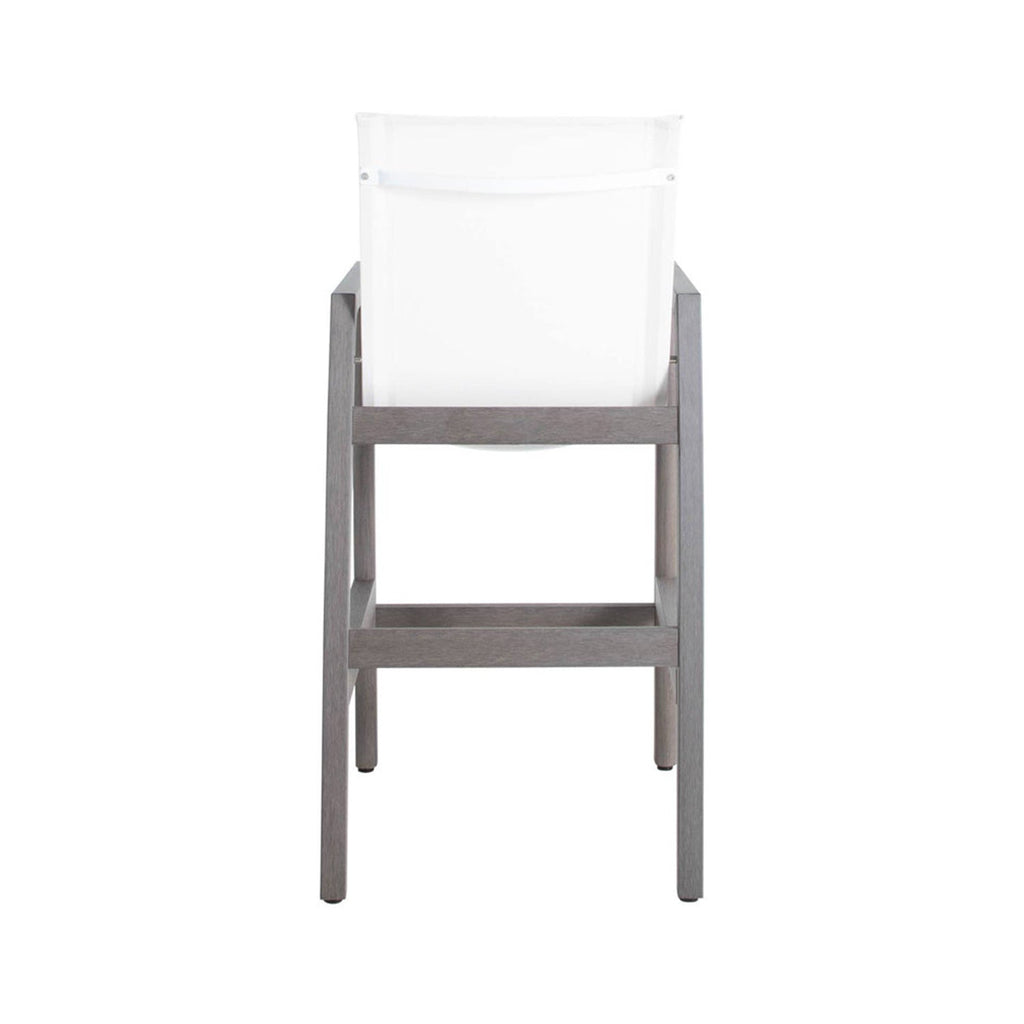 Rear view of a coastal teak outdoor bar stool with a white sling back, teak wood frame, straight legs and a built-in horizontal footrest.