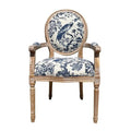 French-style dining armchair with carved teak frame in a natural distressed finish and round medallion back, upholstered in cream linen with a blue toile bird and floral pattern, padded seat and upholstered armrests.