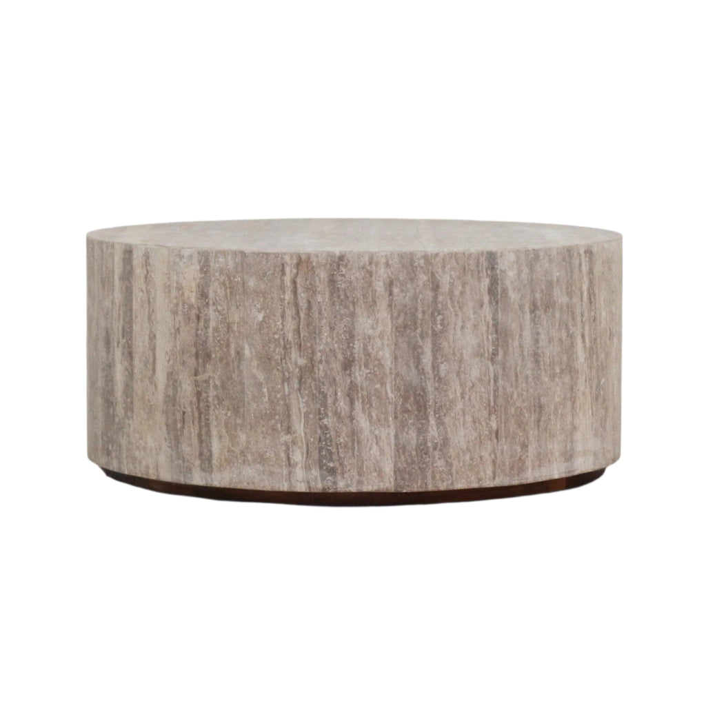 Round drum-style coffee table crafted from natural travertine marble in beige tones, showing vertical stone veining and a thin dark low base for a modern contemporary living room.