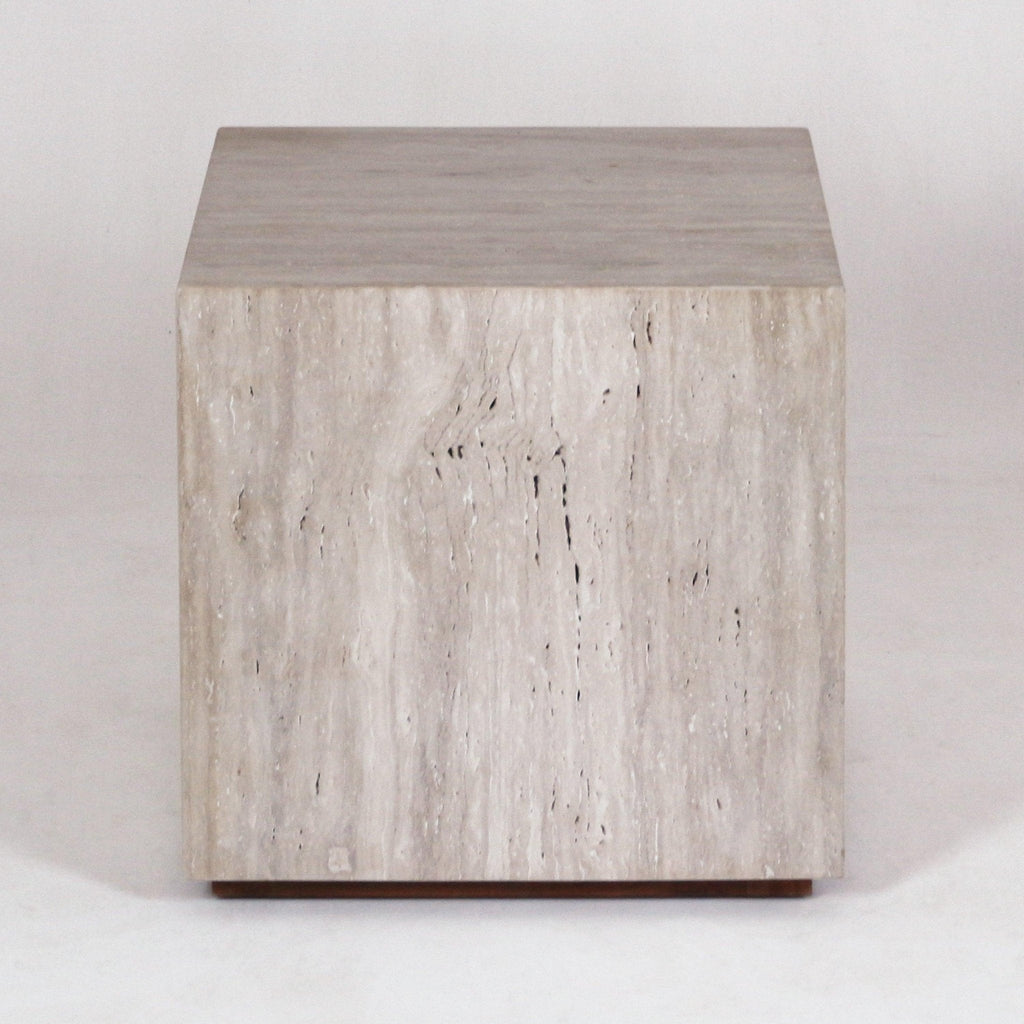 Front-facing view of a modern cube-shaped nightstand carved from natural travertine marble with neutral beige stone veining and a low wooden plinth base.