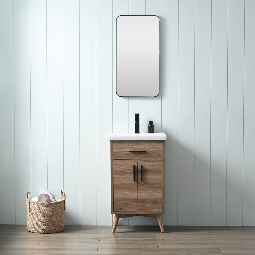 Freestanding modern solid wood bathroom vanity in natural walnut with a white ceramic sink, black faucet and matching black handles, rounded rectangular mirror above and woven towel basket against a pale shiplap wall.