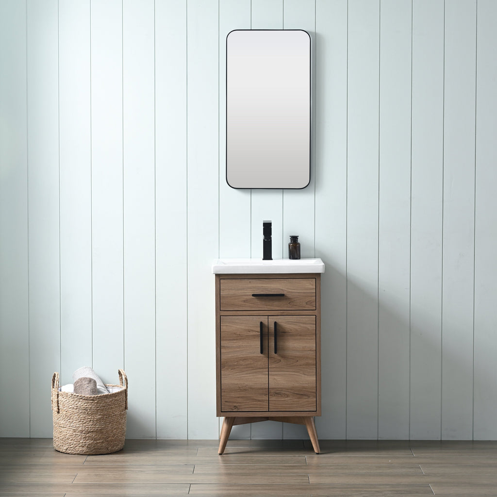 Freestanding modern solid wood bathroom vanity in natural walnut with a white ceramic sink, black faucet and matching black handles, rounded rectangular mirror above and woven towel basket against a pale shiplap wall.
