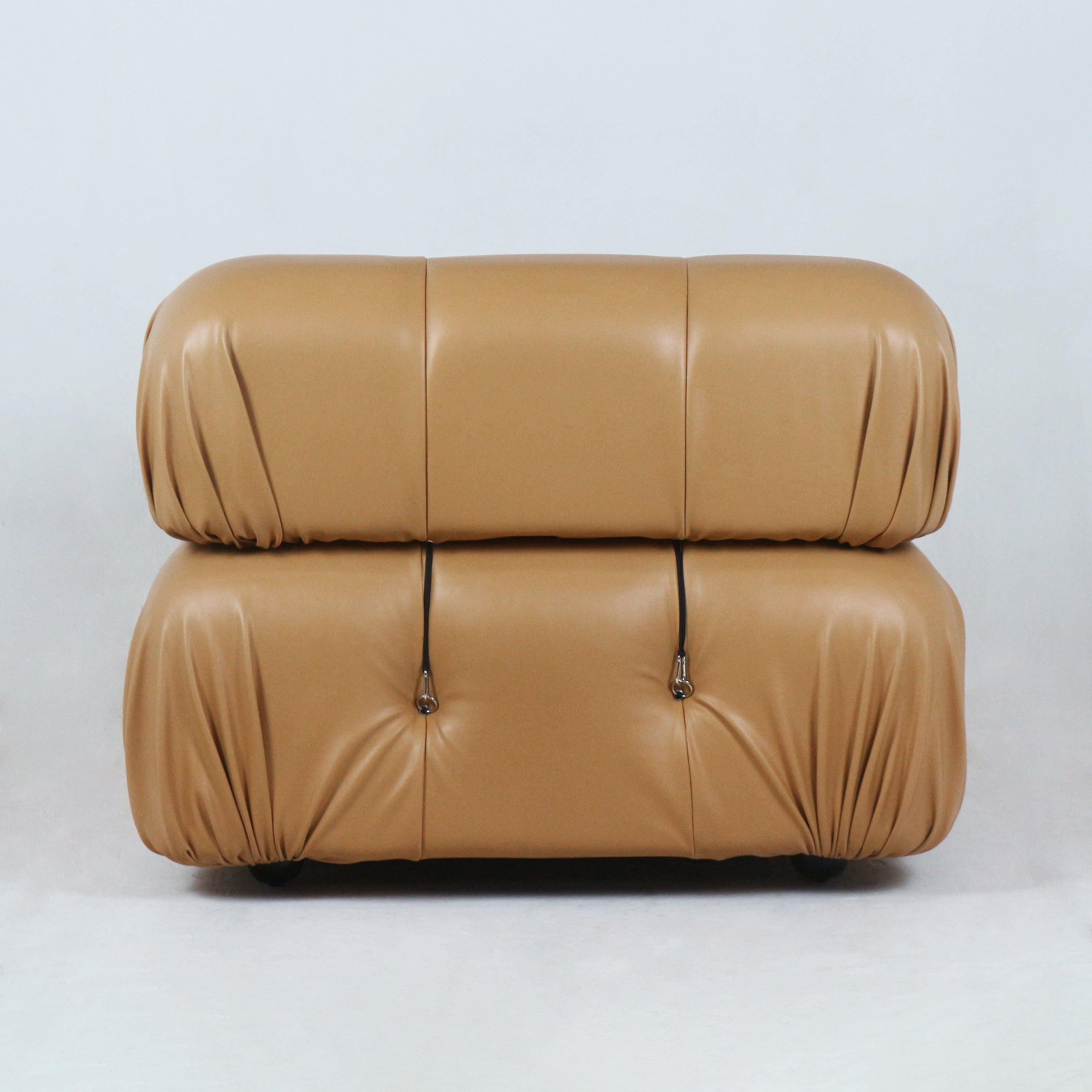Front view of a tan leather modern sofa with two stacked rounded cushions, gathered corner pleats, tufted buttons with metal strap hardware and a low profile on short feet.