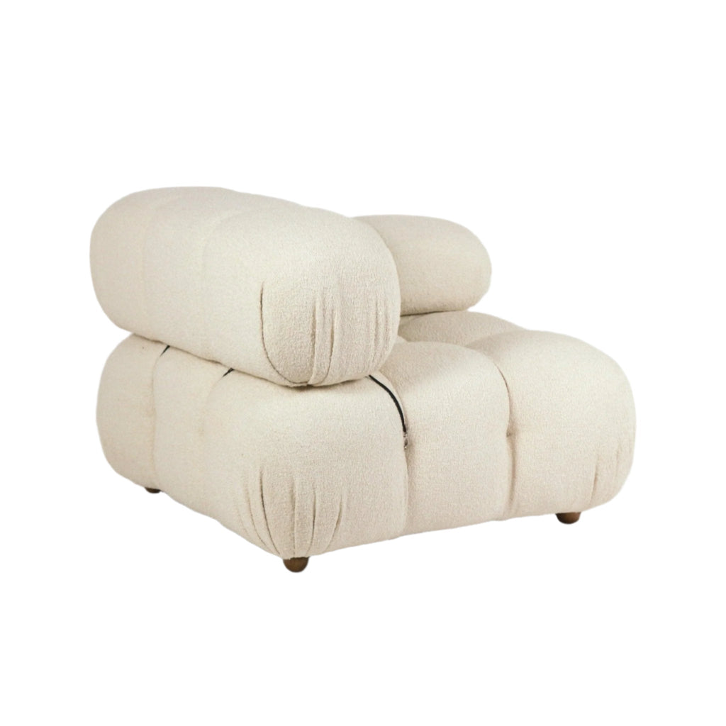 Cream boucle upholstered armless lounge chair with oversized rounded tufted cushions and low wooden legs, shown on a white background in a sculptural modern style.