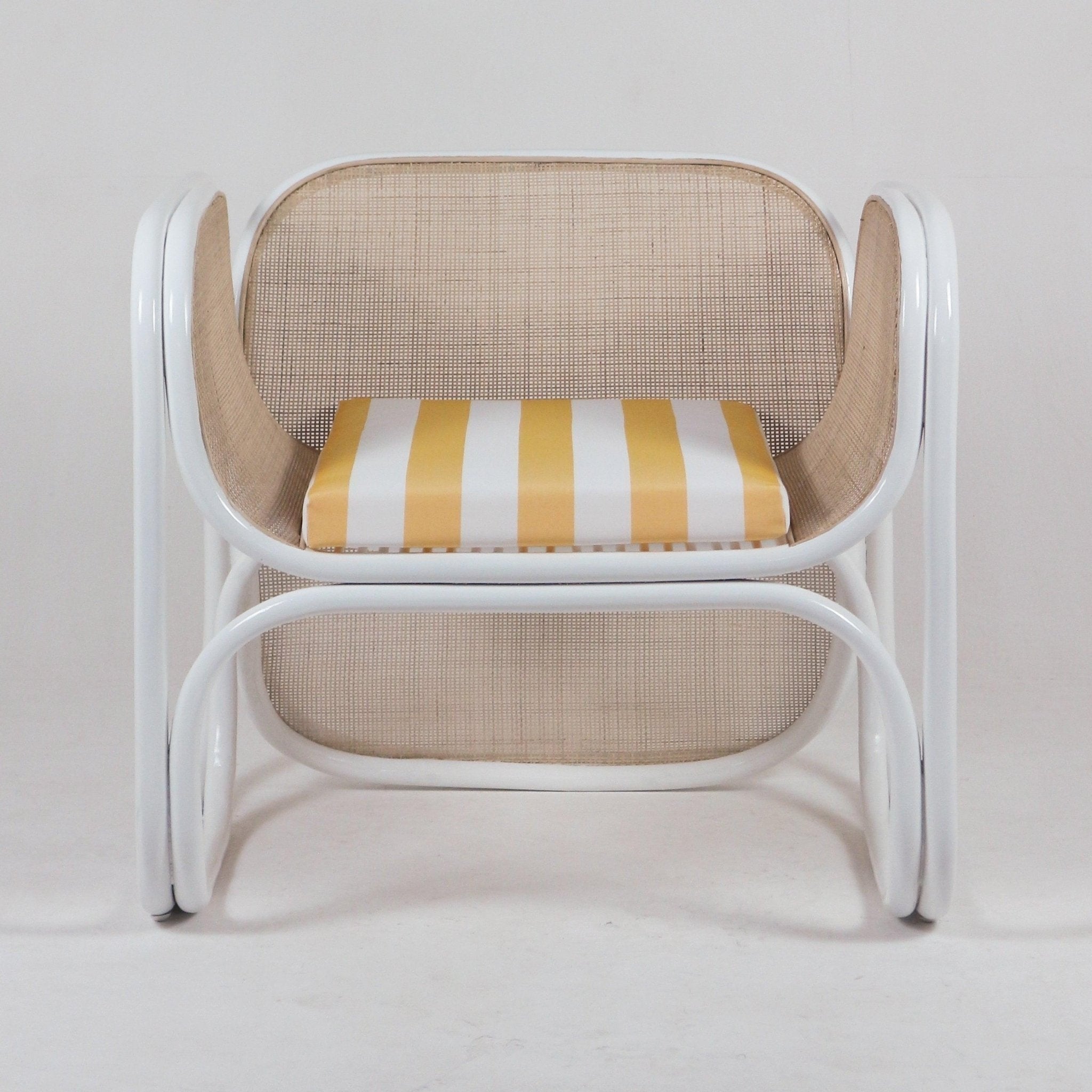 Modern cane lounge chair with curved white metal frame, natural woven cane back and sides, and a yellow-and-white striped fabric seat cushion.