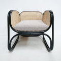 Front view of a modern lounge chair with a black curved bentwood frame, natural woven cane back and sides, and a light gray fabric seat cushion.