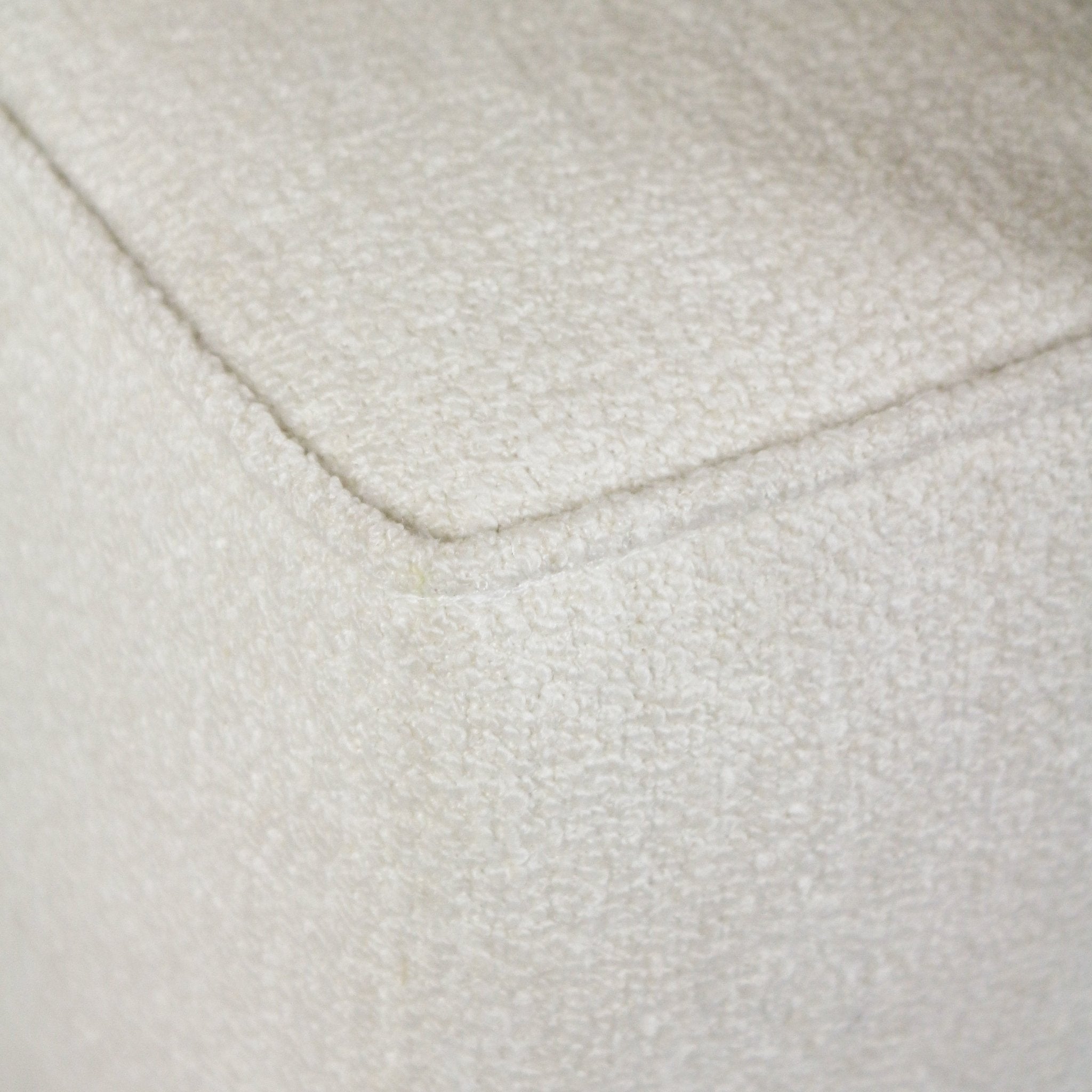 Close-up of a cream boucle upholstered bench corner showing looped fabric texture and a neat piped seam.