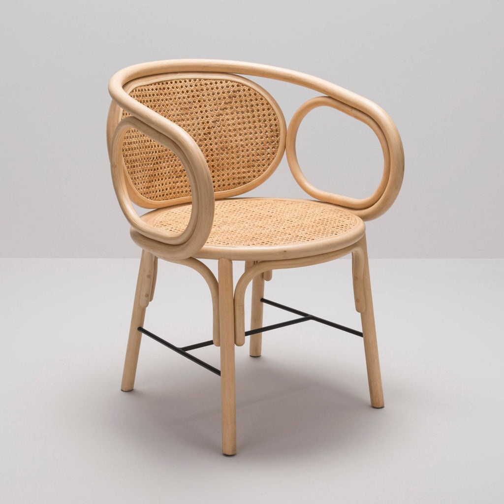 Natural rattan dining chair with bent natural wood frame and cane-woven round back and seat, curved open armrests and black metal cross-stretcher, boho-style indoor dining chair.
