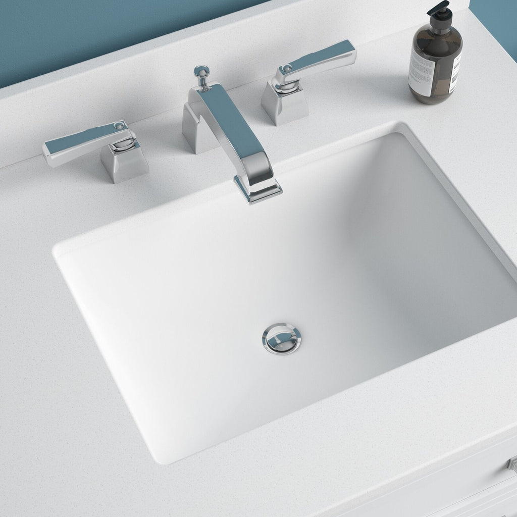 Top-down view of a modern stone-colored vanity top with a white rectangular undermount sink, chrome widespread faucet with lever handles, and a brown pump soap bottle on the countertop.