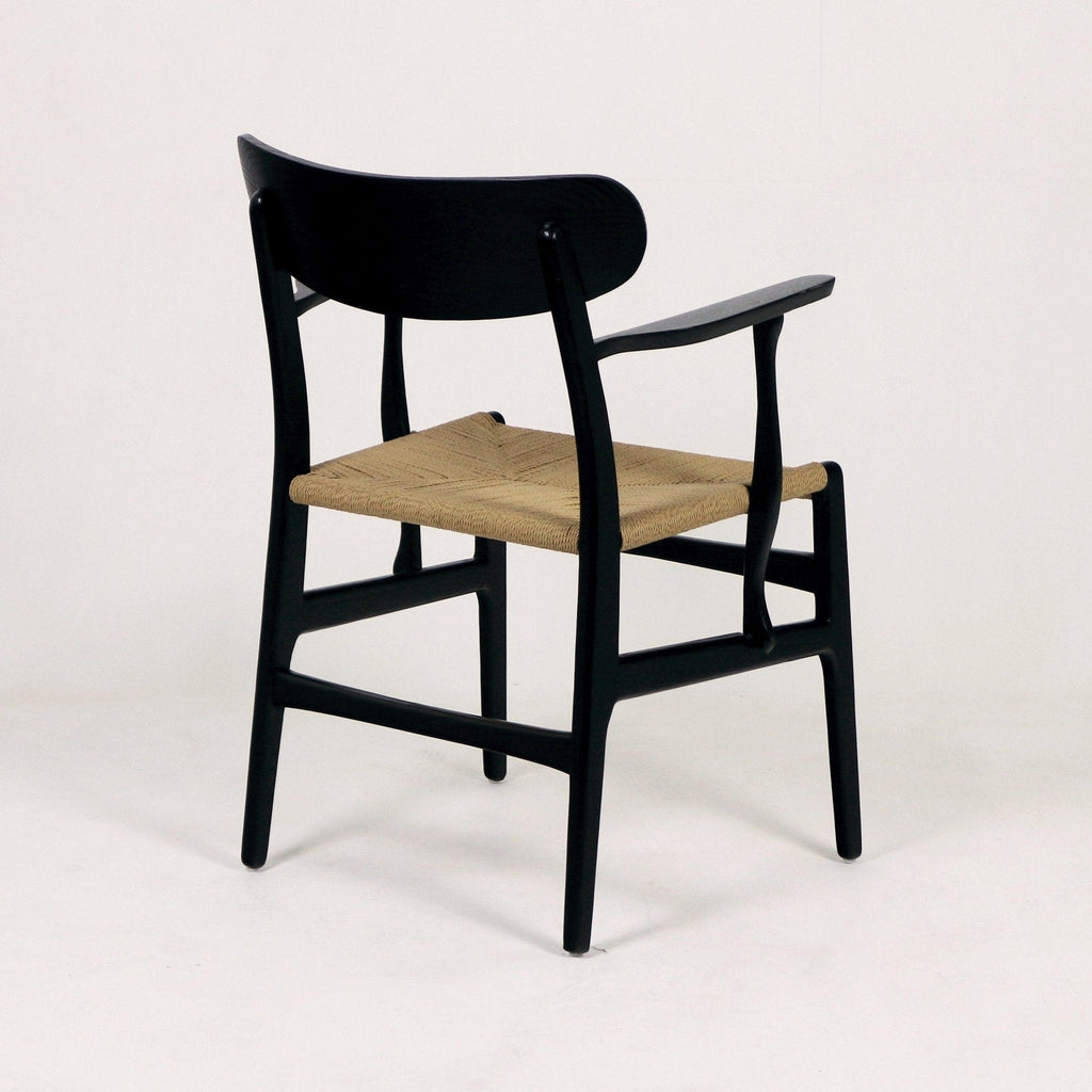 Modern black solid wood dining chair with curved back, slender armrests and woven natural rope seat, shown three-quarter rear view on a white studio background.