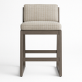 Front view of an armless teak outdoor bar stool with a beige textured fabric seat and low upholstered back, rectangular teak frame and horizontal footrest in a contemporary coastal style.