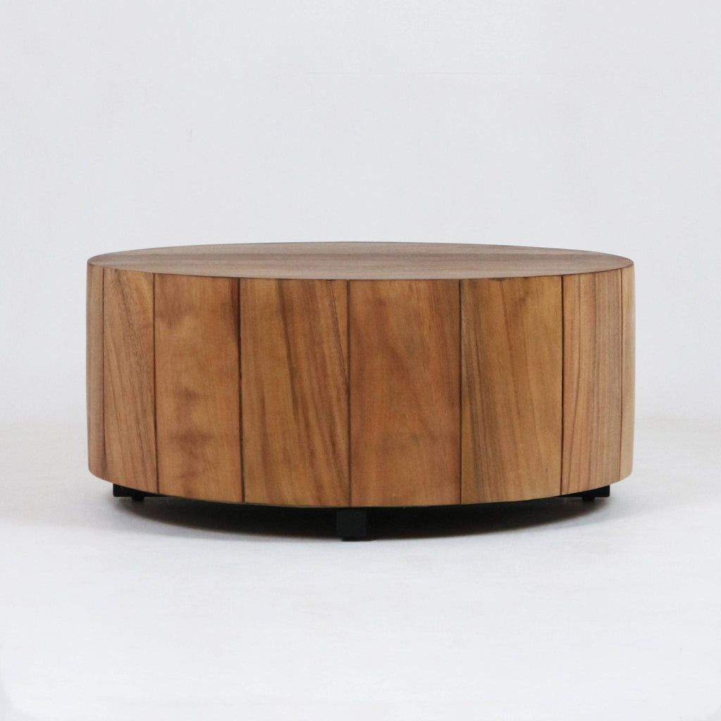 Low, round solid wood coffee table with vertical plank panels and a natural brown finish, supported by a low black metal base against a plain white background.