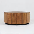 Low, round solid wood coffee table with vertical plank panels and a natural brown finish, supported by a low black metal base against a plain white background.