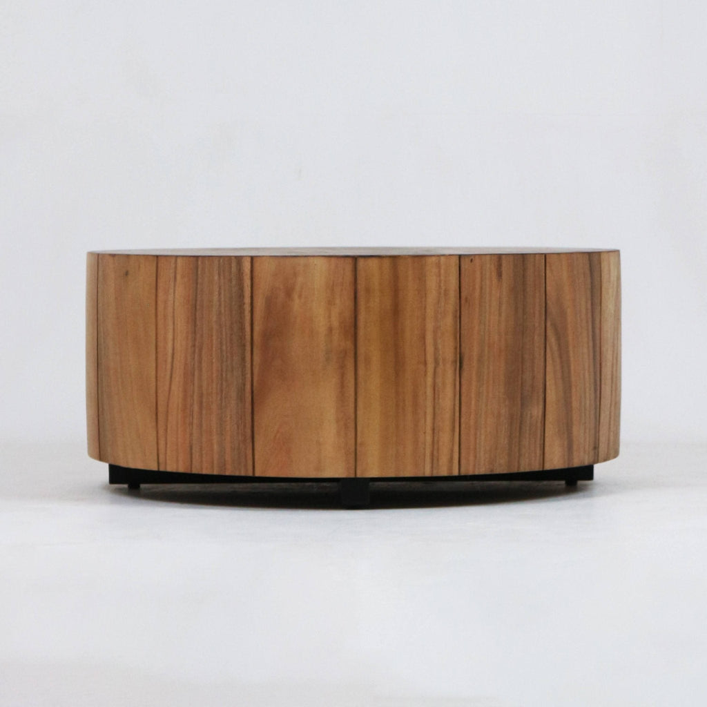 Low round solid wood coffee table with vertical plank panels and visible natural wood grain, supported by a recessed black metal base in a modern minimalist style, photographed on a white background.