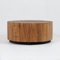Low, round solid wood coffee table with vertical plank panels and a natural brown finish, supported by a low black metal base against a plain white background.