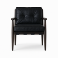 Front view of a mid-century modern dining chair upholstered in black aged nubuck leather with a two-button tufted back, plush seat cushion, and walnut-stained tapered wooden frame with armrests and exposed strap supports.