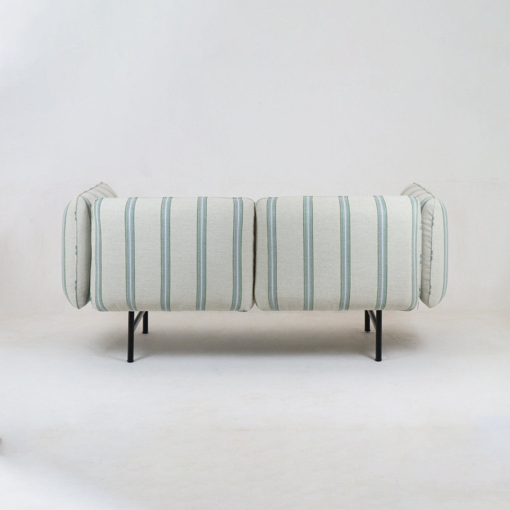Back view of a modern coastal outdoor sectional upholstered in light neutral fabric with pale green-blue vertical stripes, supported on slim black metal legs.