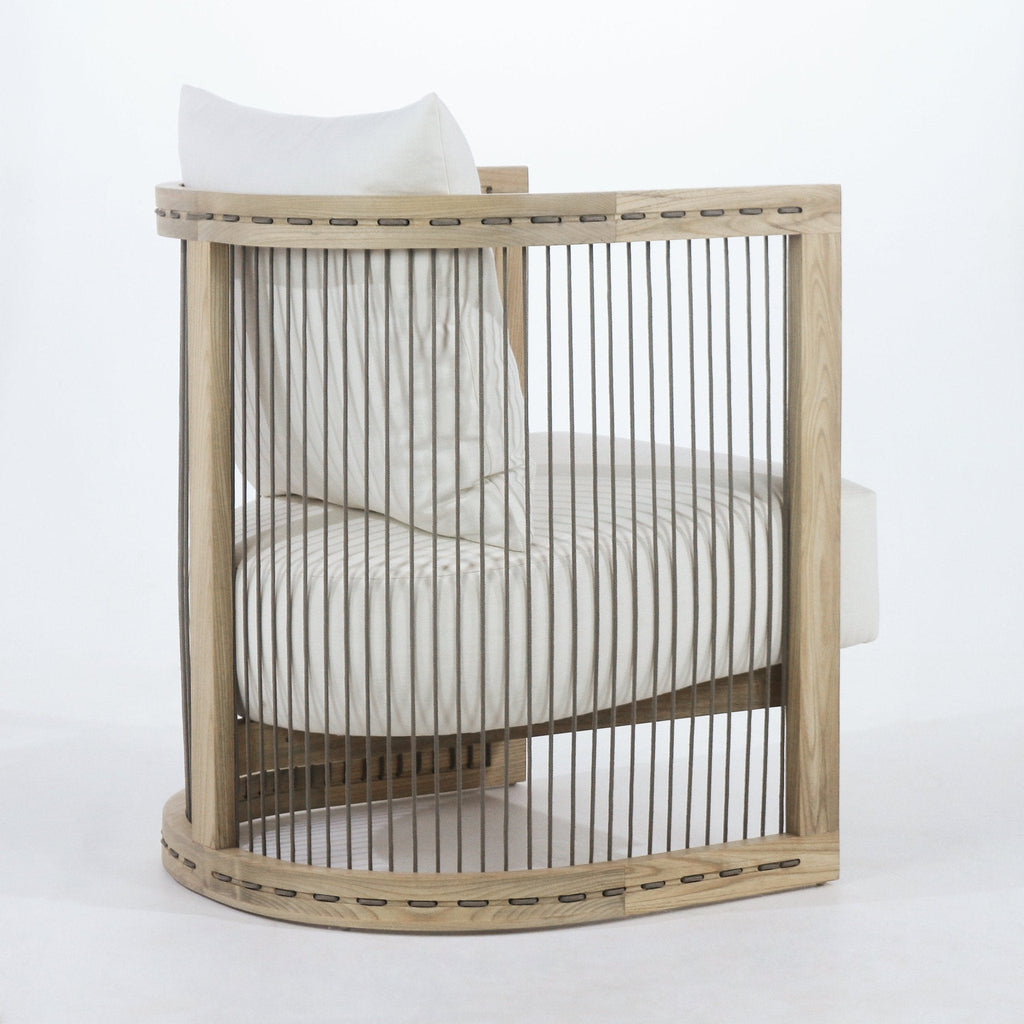 Side view of a contemporary dining armchair with a curved natural oak frame and vertical rope slats, upholstered in white fabric with a thick cushioned seat and a loose white back pillow.