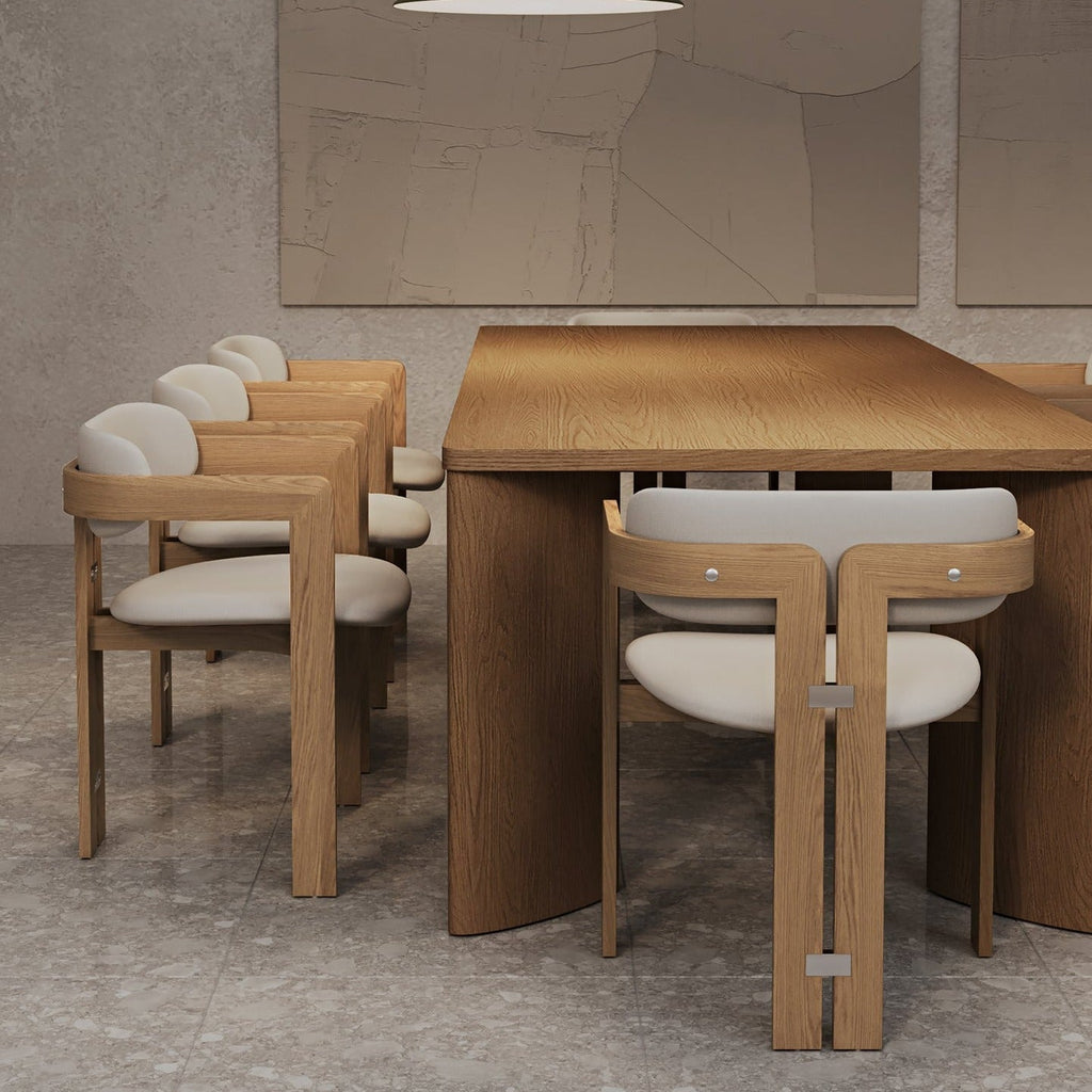 Mid-century modern teak dining table flanked by teak-framed dining chairs upholstered in off-white boucle with metal accent hardware, arranged in a neutral dining room on a stone tile floor.