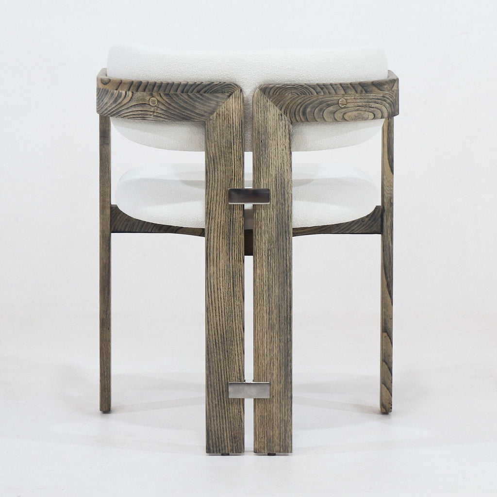 Rear view of a rustic brown stained wood dining chair with cream boucle upholstered cushioned seat and back, integrated curved arms and two small metal rectangular connectors on the vertical rear slats.