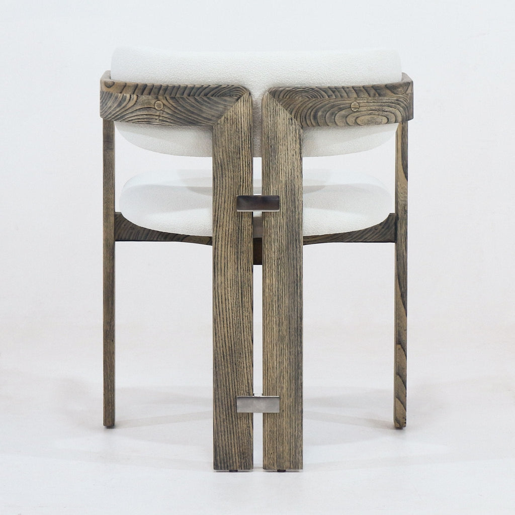 Rear view of a rustic brown stained wood dining chair with cream boucle upholstered cushioned seat and back, integrated curved arms and two small metal rectangular connectors on the vertical rear slats.