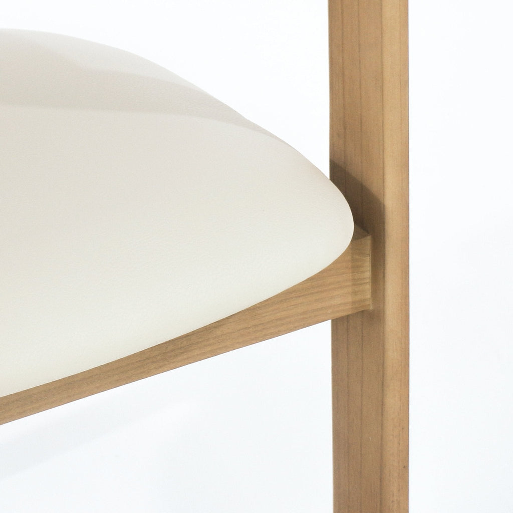 Close-up of a beige leather upholstered dining chair seat showing the rounded cushion edge and the natural teak wood frame and vertical leg with visible wood grain.