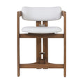 Front view of an outdoor teak-framed bar stool with curved arm supports and off-white fabric seat and low back, showing metal bracket hardware and an integrated wooden footrest in a coastal contemporary style.
