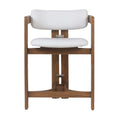 Front view of an outdoor teak-framed bar stool with curved arm supports and off-white fabric seat and low back, showing metal bracket hardware and an integrated wooden footrest in a coastal contemporary style.