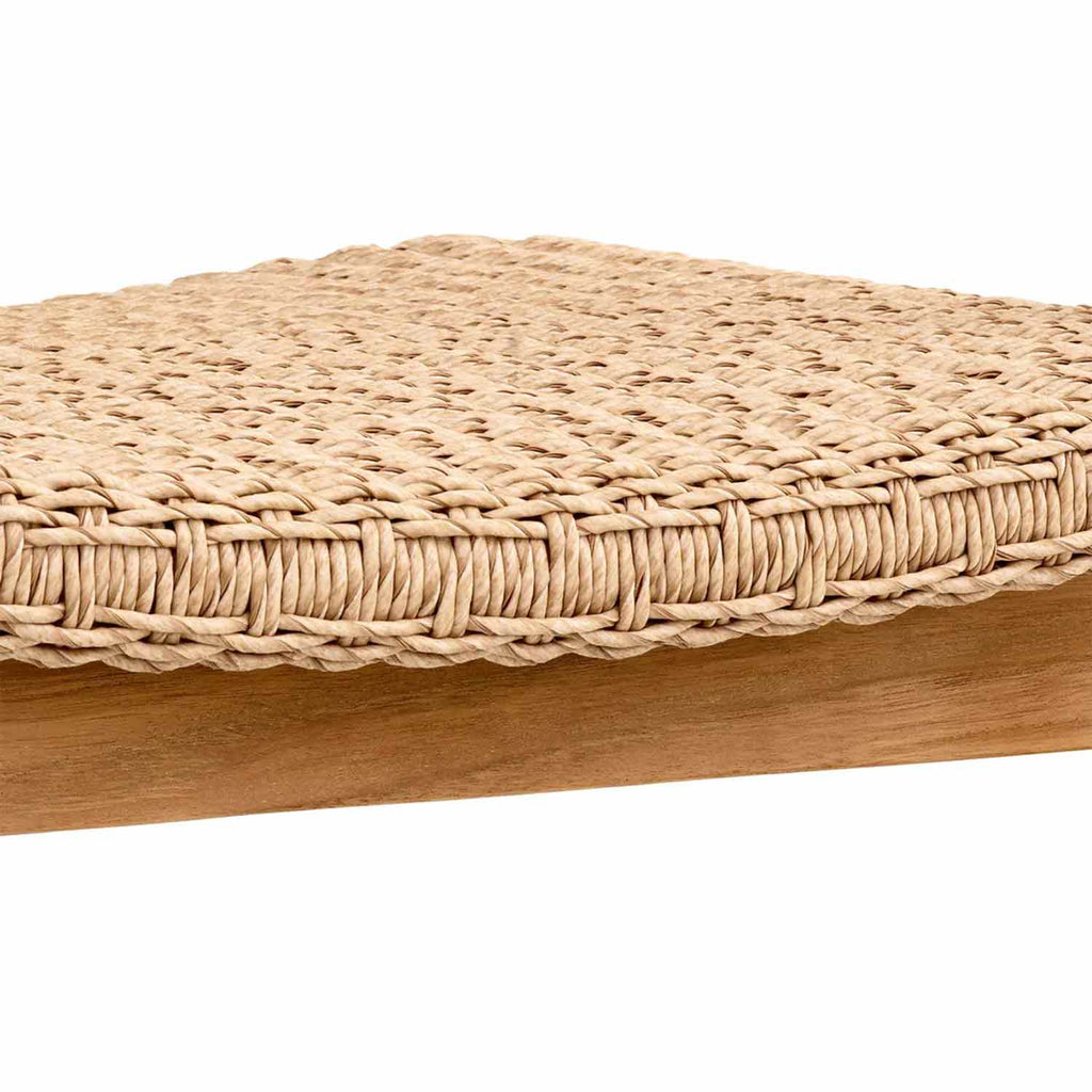 Close-up of a natural teak dining chair showing a tightly woven beige synthetic-fiber seat with braided edging above a smooth teak wood frame.