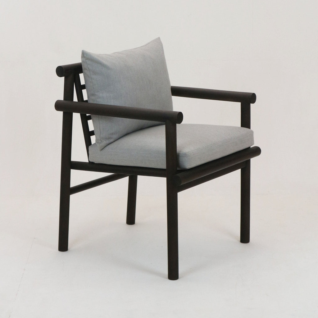 Dark teak wood patio armchair with cylindrical round-rail frame, light gray Sunbrella-upholstered seat cushion and loose back pillow in a coastal-modern design.