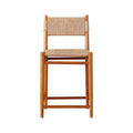 Front view of an armless teak bar stool with natural woven fiber seat and back, clean-lined coastal modern farmhouse frame and integrated footrest.