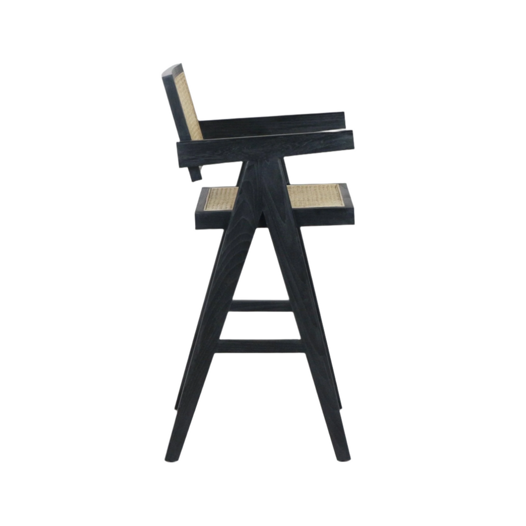 Side view of a black-stained wooden bar stool with woven natural rattan seat and back, A-frame tapered legs, integrated armrests and a footrest in a mid-century modern style.