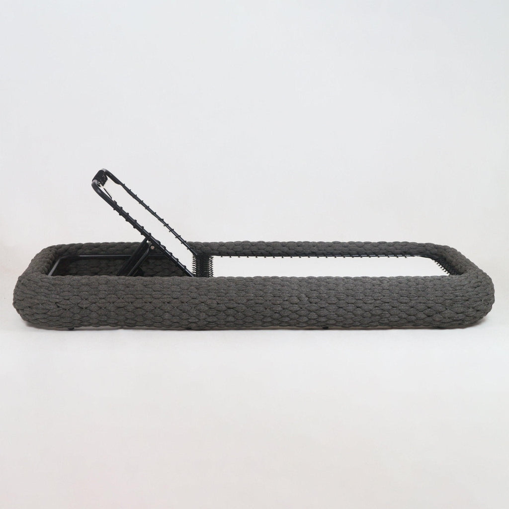 Side view of a taupe rope-woven outdoor chaise lounger with chunky braided rope frame, white fabric sling seat and black metal adjustable backrest partially raised on a white background.