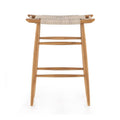 Backless teak outdoor bar stool with natural woven seat, tapered legs and two horizontal foot rails in a coastal Scandinavian style, shown on a white background.