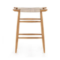 Backless teak outdoor bar stool with natural woven seat, tapered legs and two horizontal foot rails in a coastal Scandinavian style, shown on a white background.