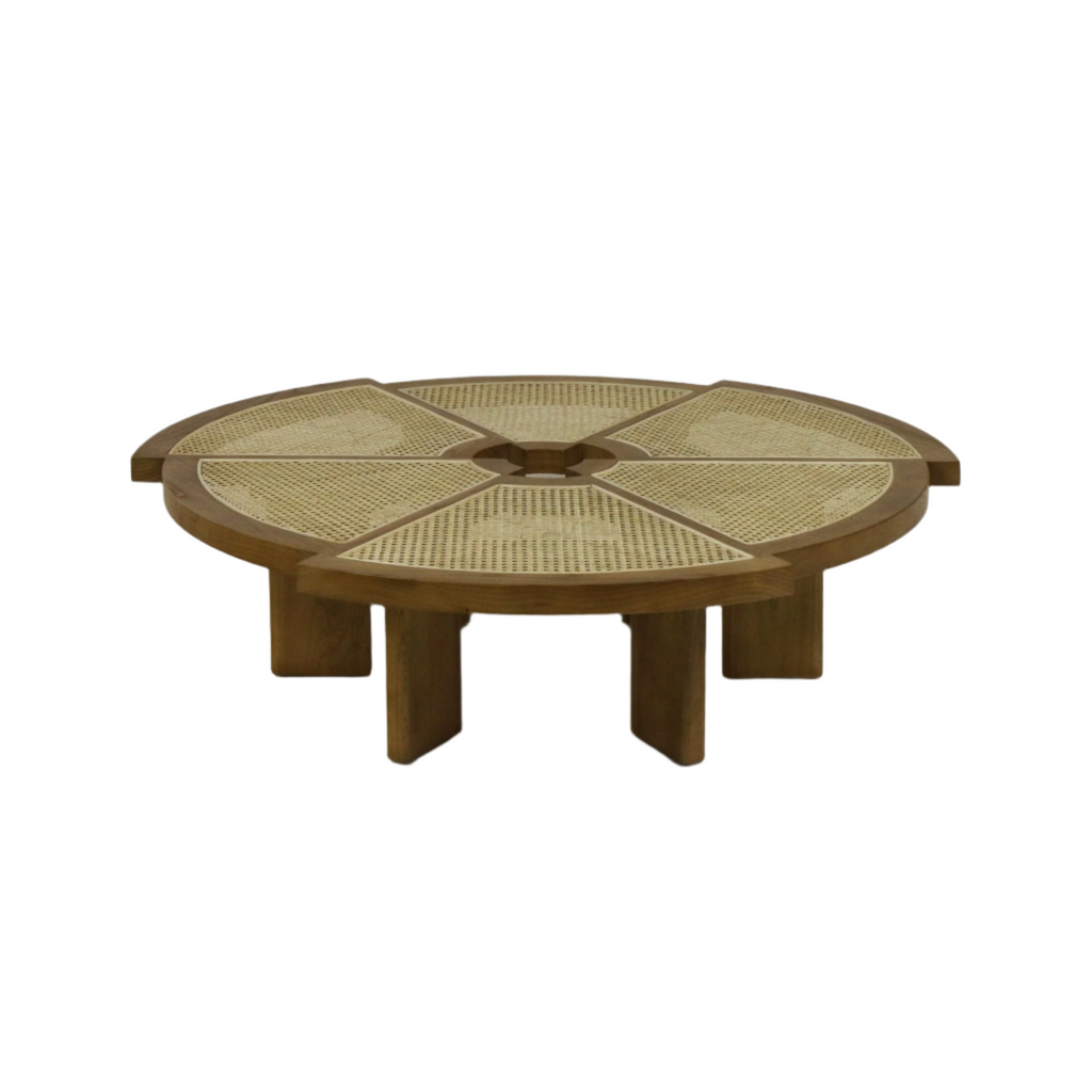 Round coffee table in natural solid wood with a cane-woven top divided into six wedge panels and a small central cutout, resting low on chunky modern-style legs.