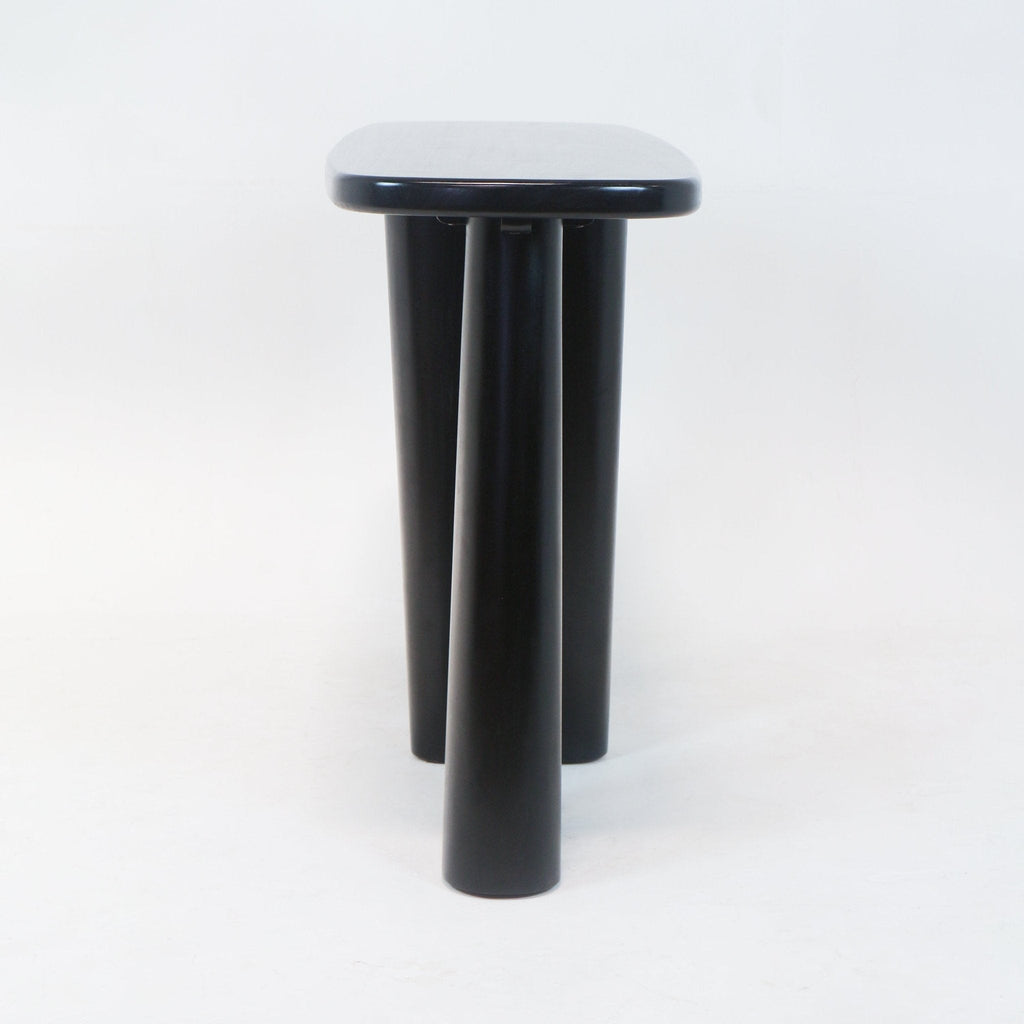 Front view of a modern solid wood console in smoked black showing a rounded rectangular top and three thick cylindrical legs against a white studio background.
