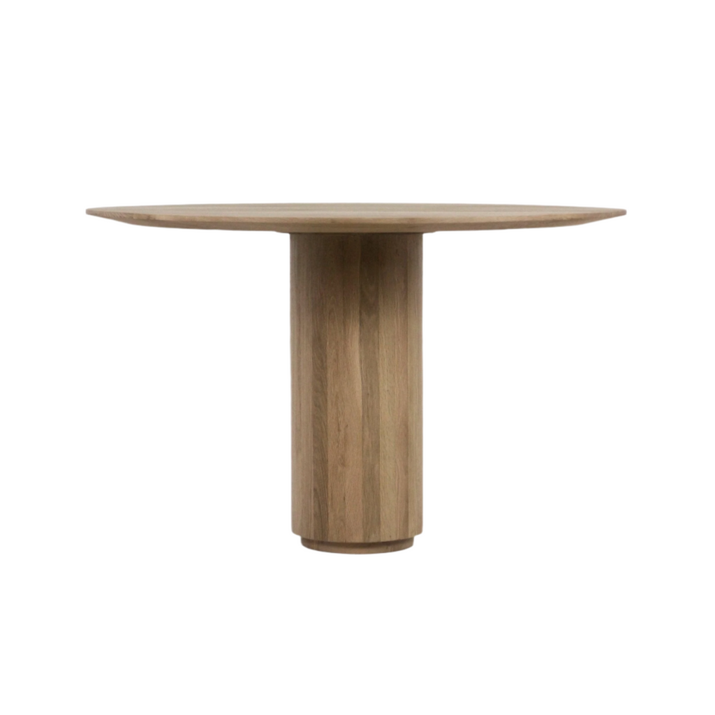 Round dining table in natural teak finish with a cylindrical pedestal base and slim solid-wood tabletop, styled in a mid-century modern aesthetic.