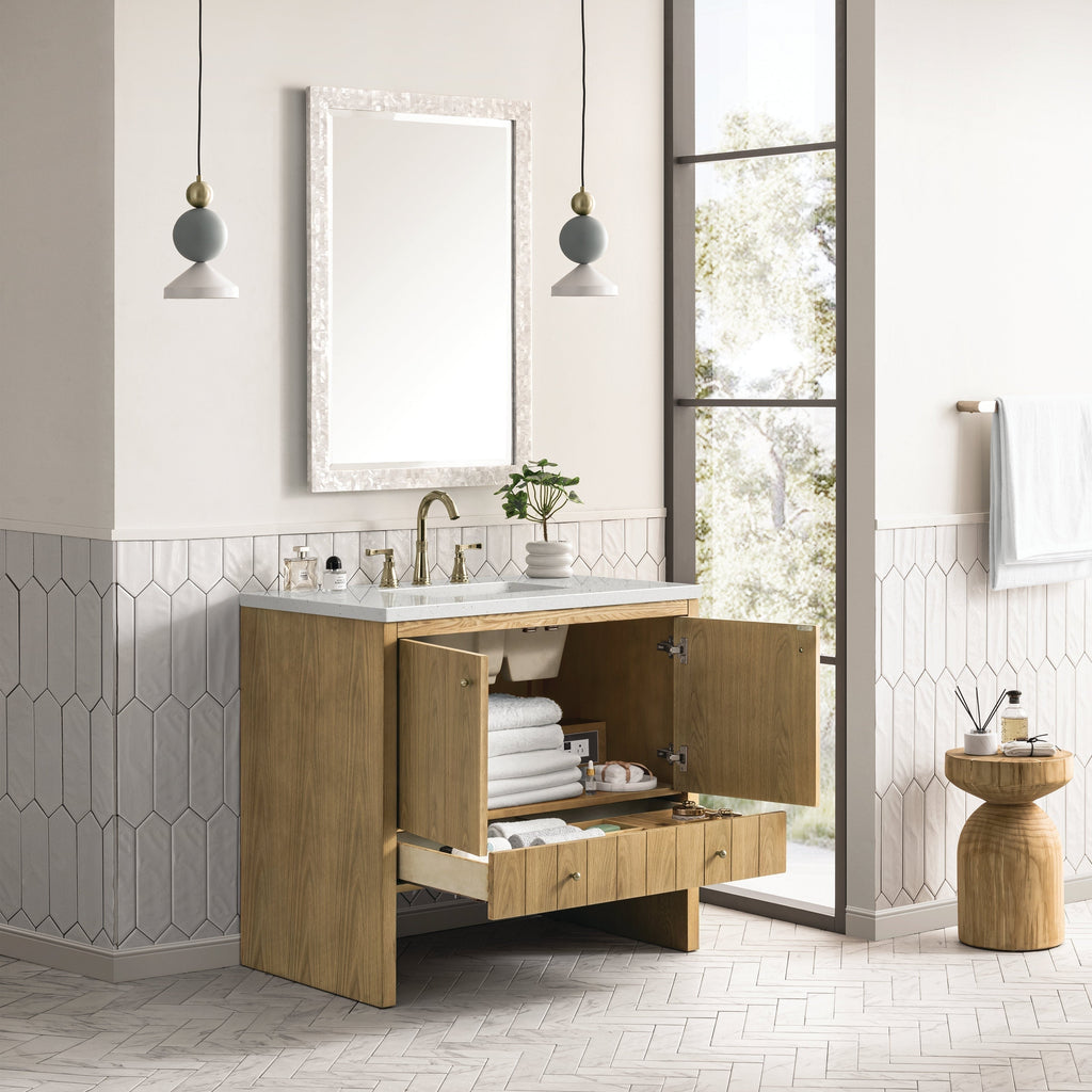 A modern bathroom features the NUEMA Sala 36 Single Bathroom Vanity with open cabinet doors and drawer displaying stacked towels and toiletries, complemented by a large mirror, stone countertop, pendant lights, and natural light.