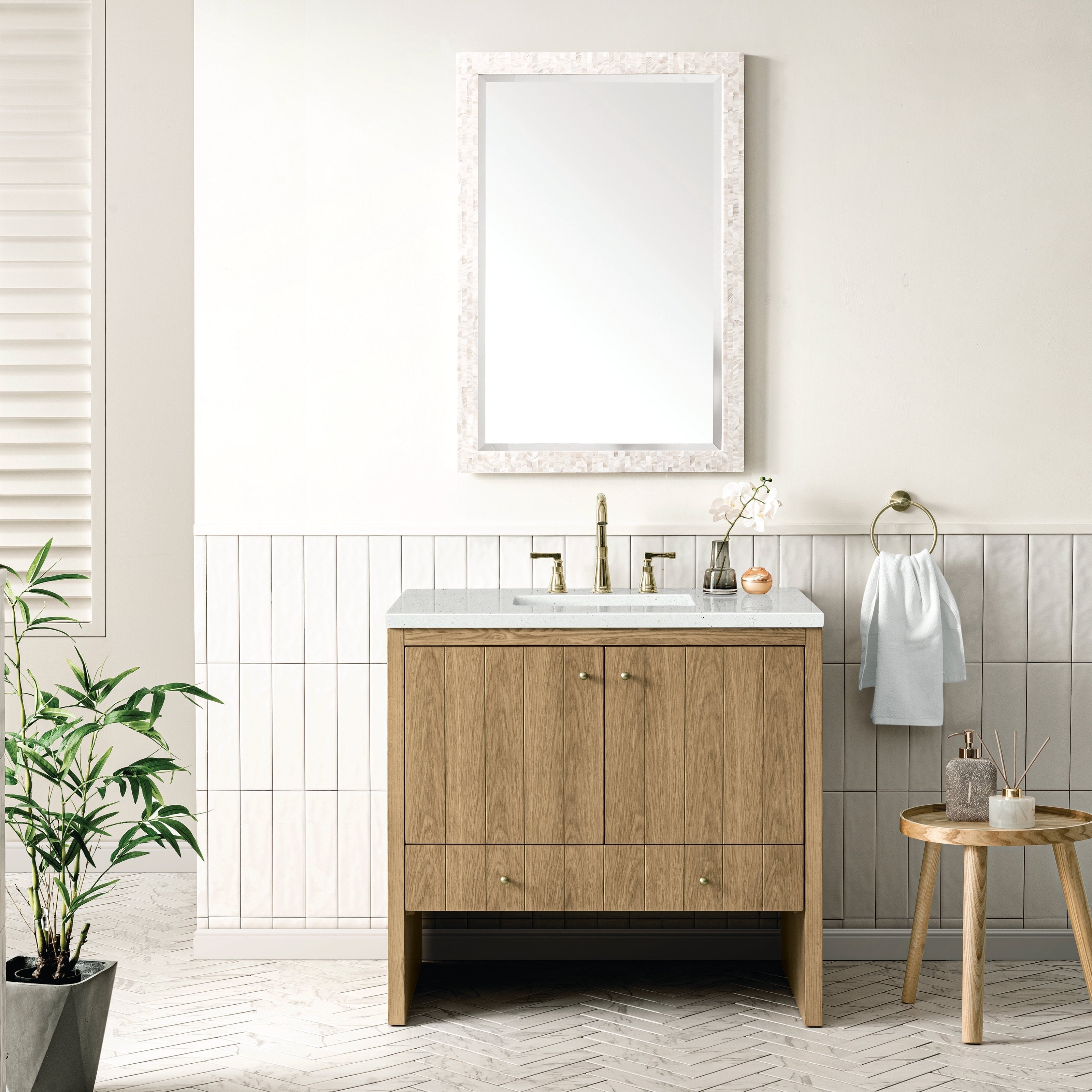 A modern bathroom features the NUEMA Sala 36 Single Bathroom Vanity with brass hardware, a stone countertop, and a rectangular mirror above. A brass faucet, towel ring, white towel, small plant, and wooden stool complete the minimalist look.