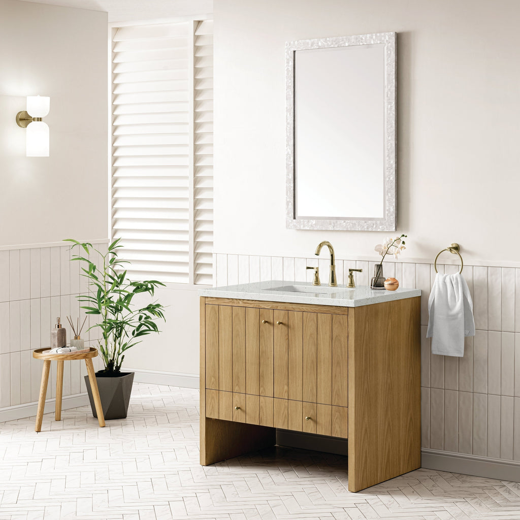 A modern bathroom features the NUEMA Sala 36 Single Bathroom Vanity with a marble countertop and brass faucet. Above, a rectangular mirror with a textured white frame hangs over light walls with white tile accents.