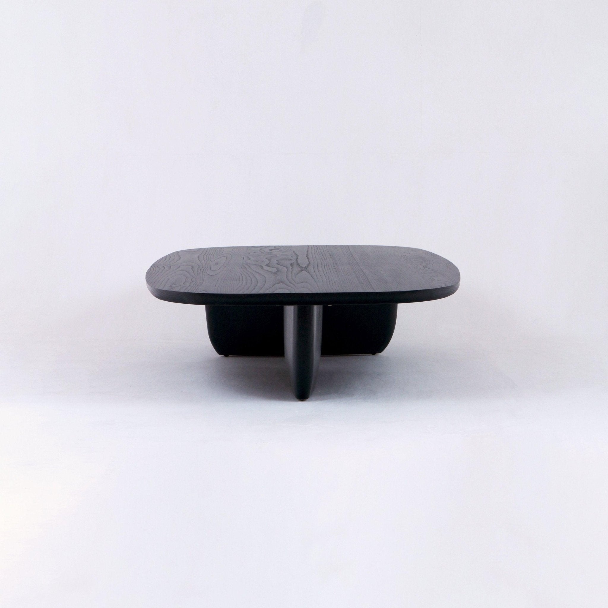 Modern low black oak coffee table with a rounded rectangular top showing subtle wood grain and a sculptural central pedestal base, photographed on a white studio background.