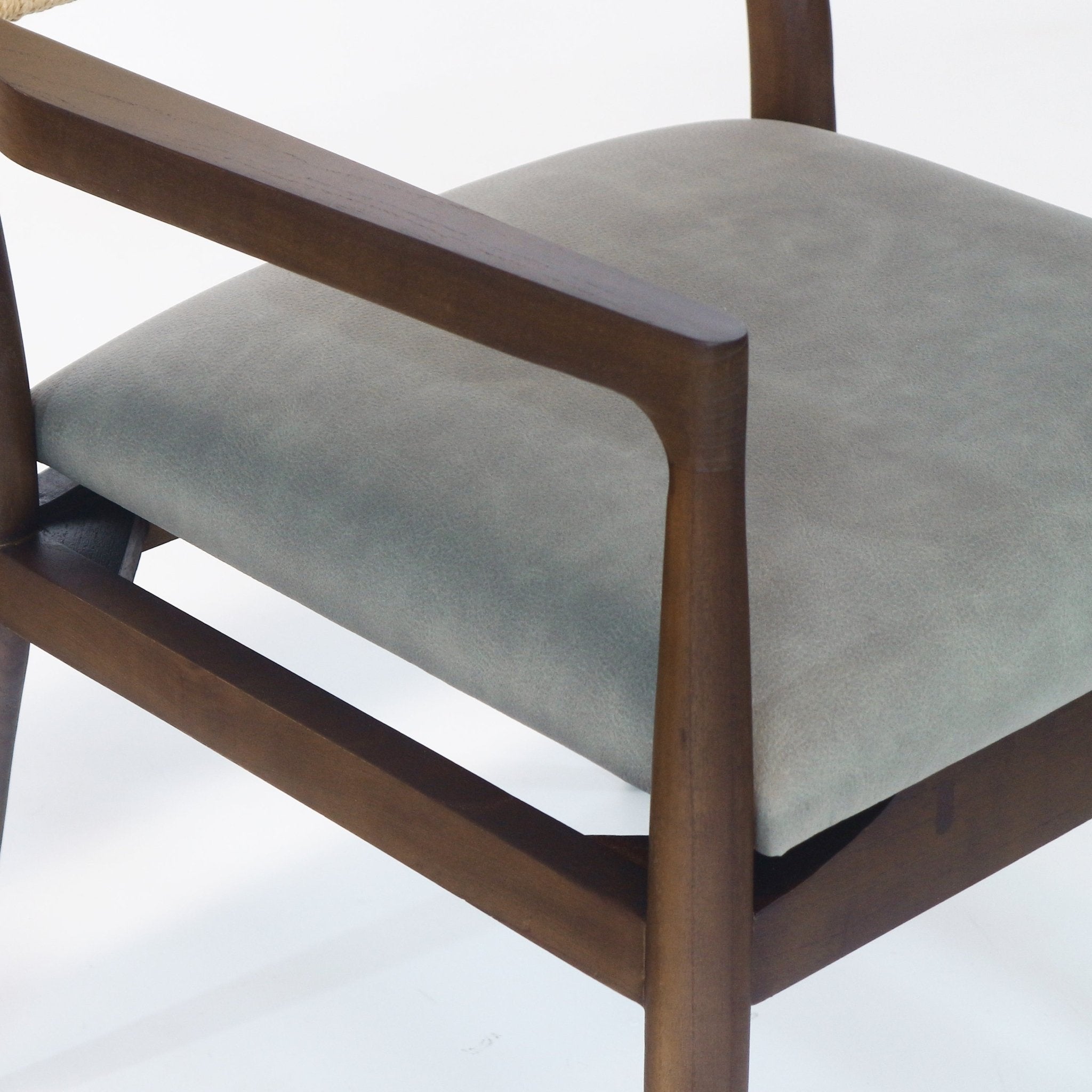 Close-up of a dining chair showing a natural wood arm and frame with a cushioned blue faux-leather seat, subtle leather texture, and a hint of the rope-wrapped backrest at the top left.