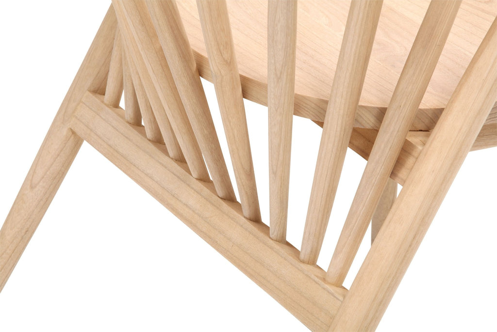 Close-up of a natural teak dining chair showing a solid wood seat, angled leg and vertical spindle back with visible wood grain in a mid-century modern style.