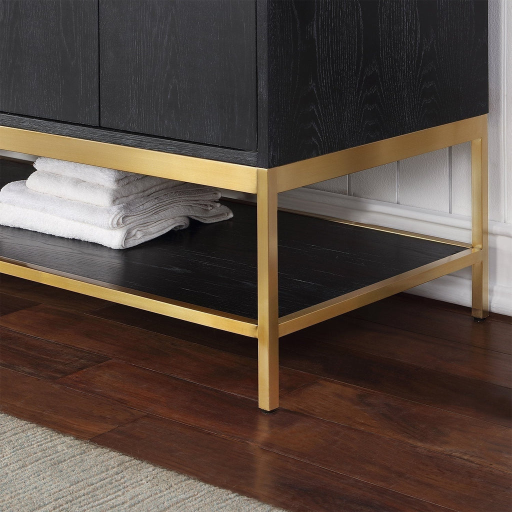Close-up of the lower corner of a modern solid wood bathroom vanity in stone finish, showing a gold metal base and open lower shelf with folded white towels on a dark hardwood floor by a white beadboard wall.