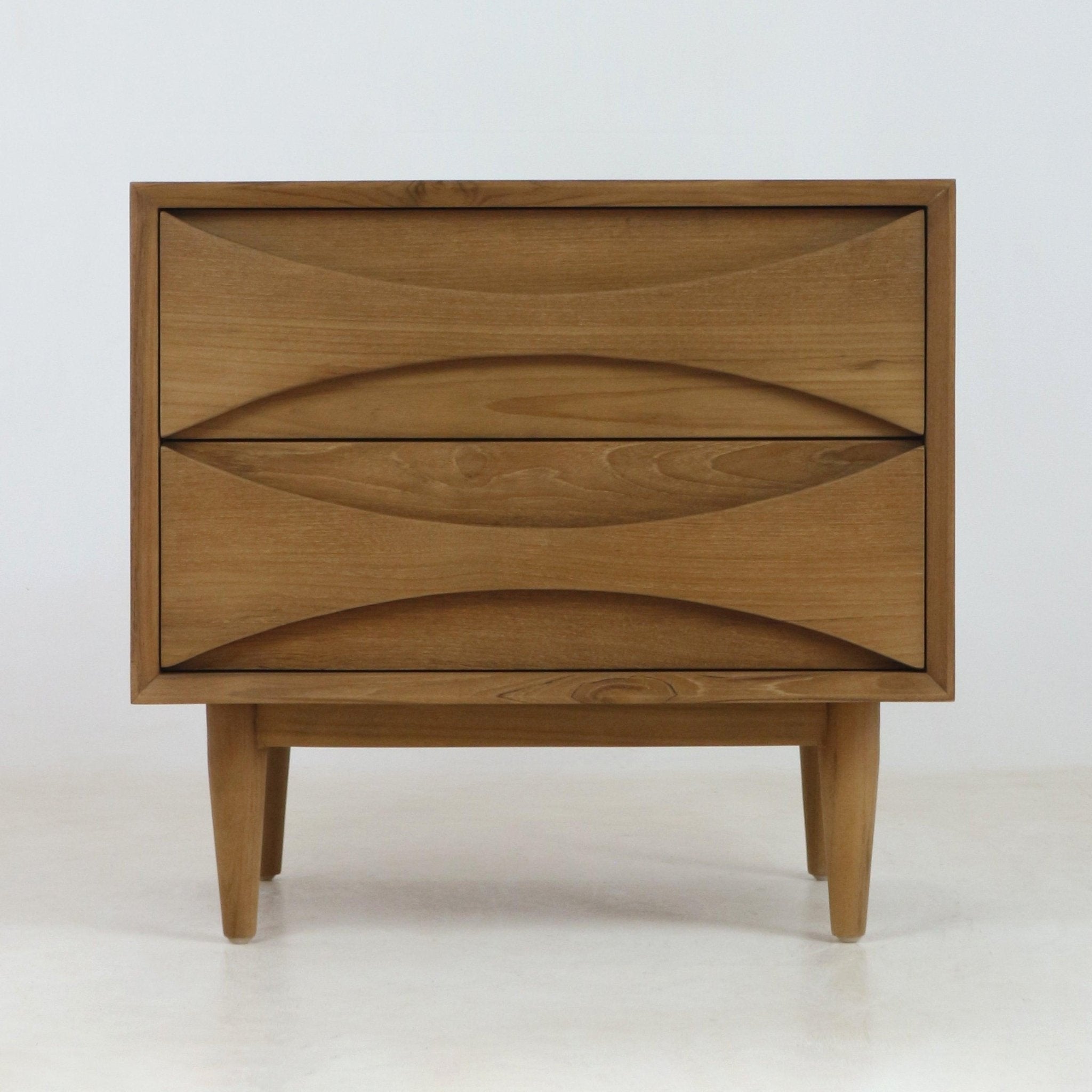 Natural teak two-drawer nightstand in mid-century Scandinavian style with carved recessed drawer pulls, tapered legs and warm wood grain finish shown on a pale neutral background.