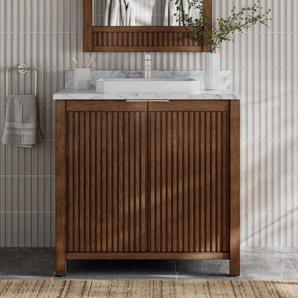 36-inch freestanding fluted solid-wood bathroom vanity in warm brown with a stone marble top, rectangular white vessel sink and single faucet, shown with a matching wood mirror, towel on ring and vase against ribbed tile.